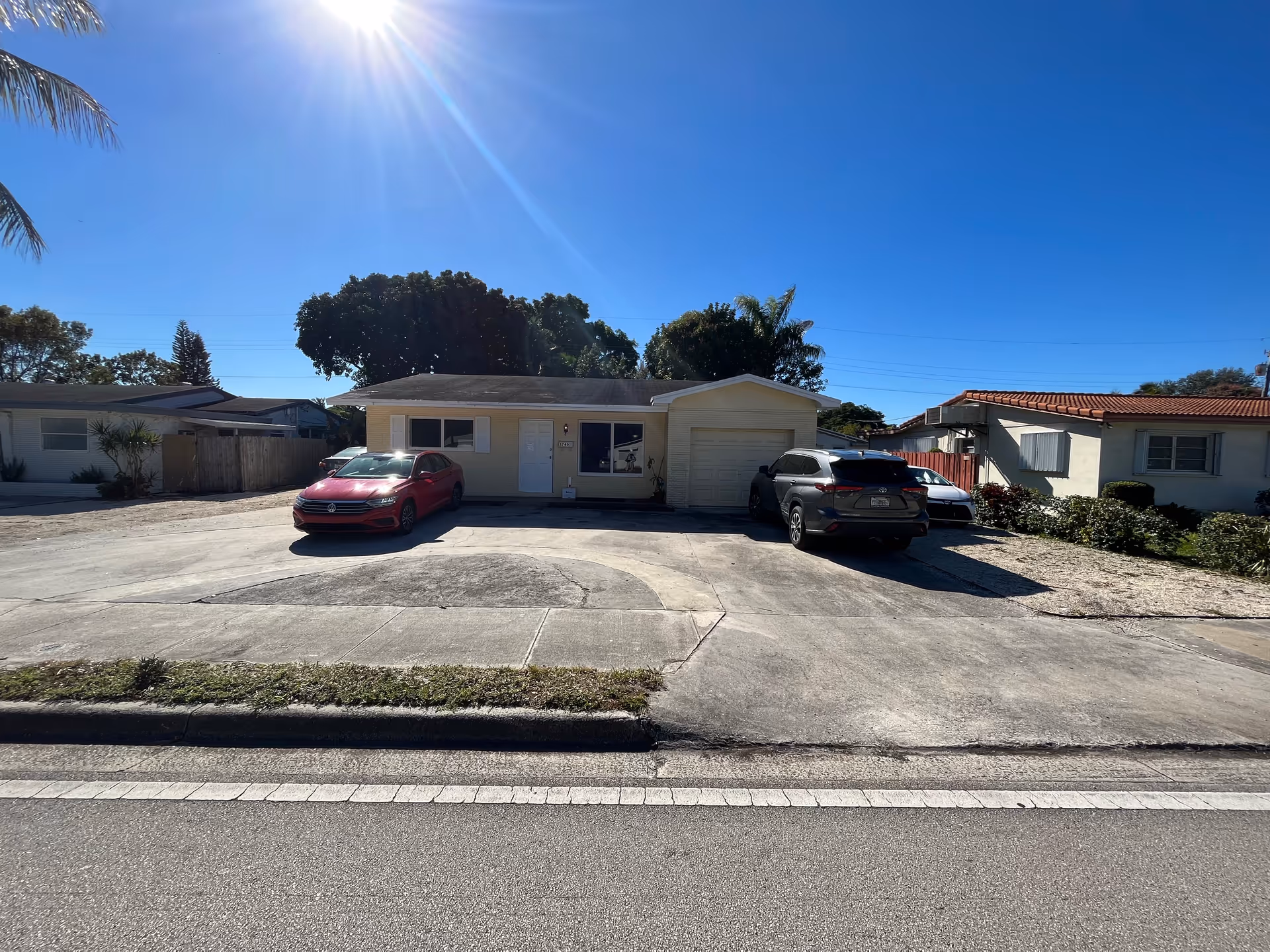Single story beige facility with a driveway, two cars, and a clear blue sky.