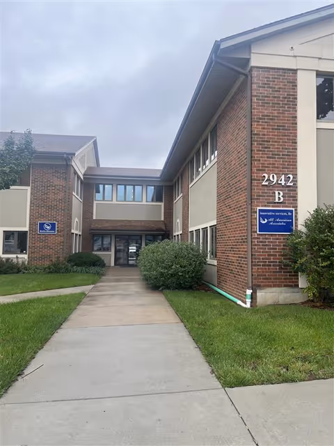 Brick senior living facility exterior with walkway leading to entrance and signs.