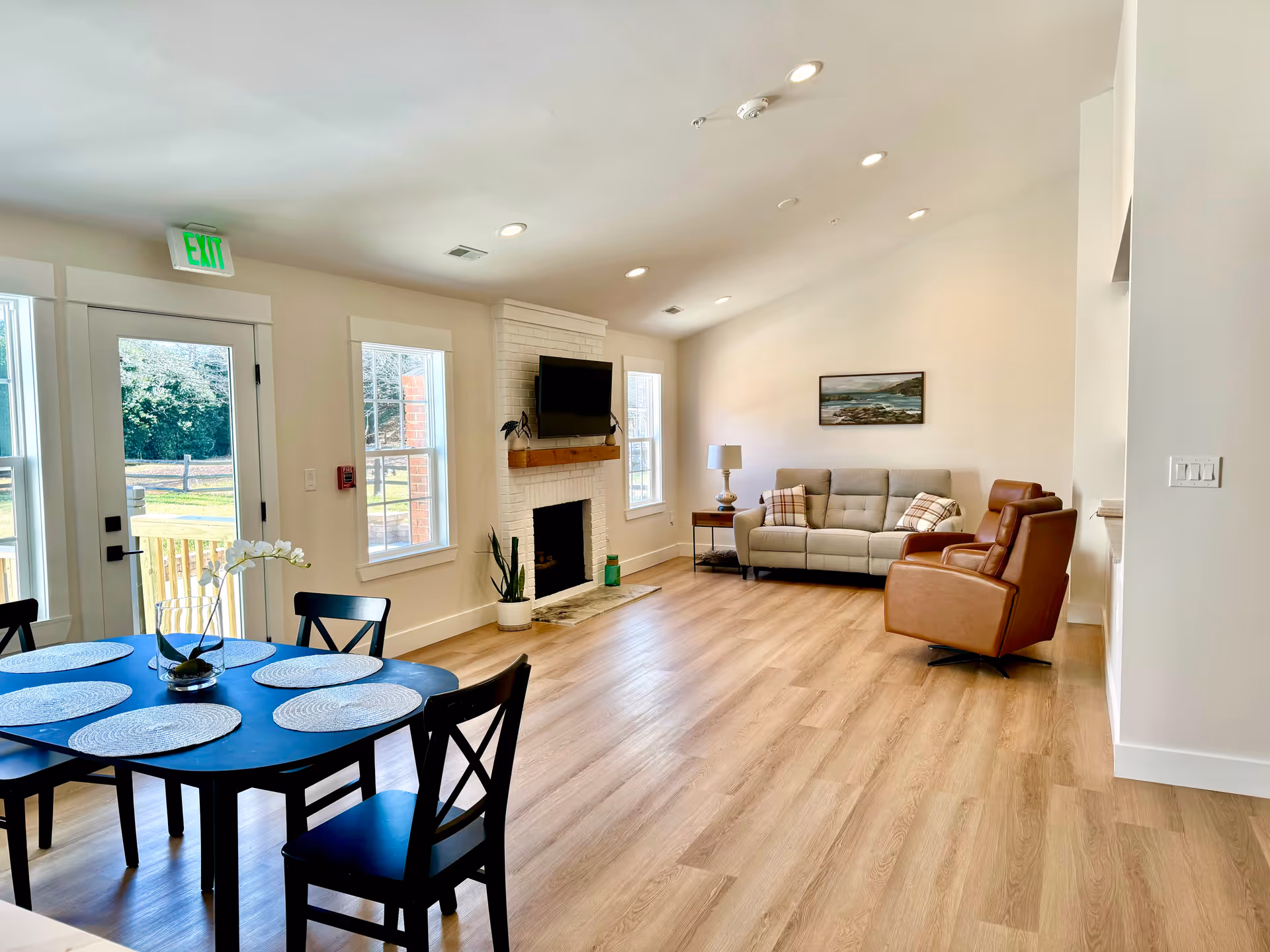 Bright open living room with sofa, leather chair, fireplace, and dining table.