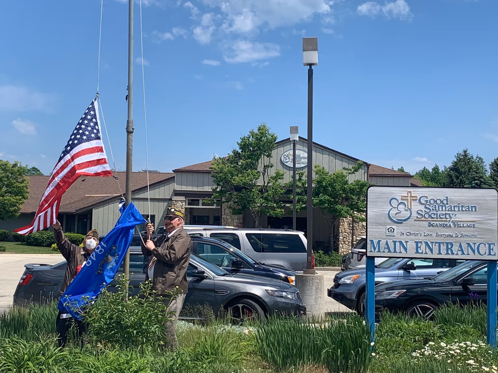 Two people raise an American flag near the Good Samaritan Society main entrance exterior.