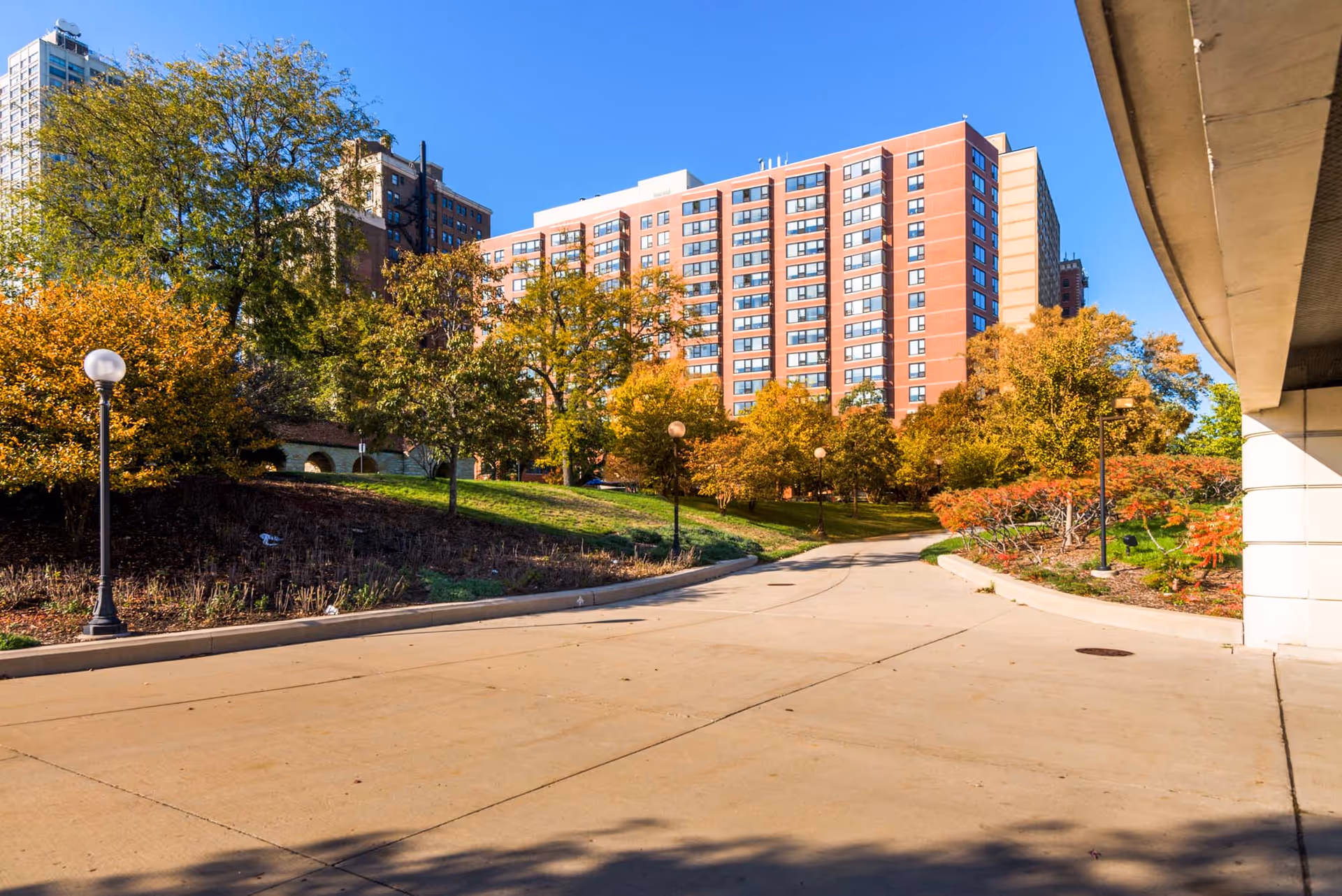 Mid-rise brick senior living building with trees, a curved driveway, and landscaped grounds.