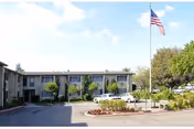 Two-story senior living building with American flag, landscaped entrance, and parked cars.