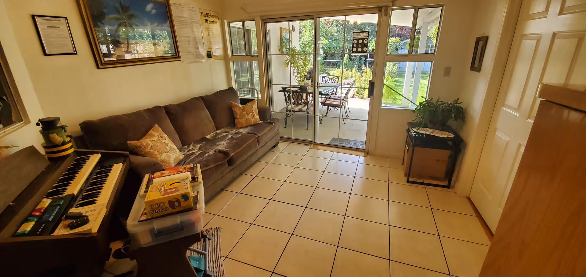 Cozy living room with brown sofa, piano, tiled floor, and glass doors to the outdoor patio.