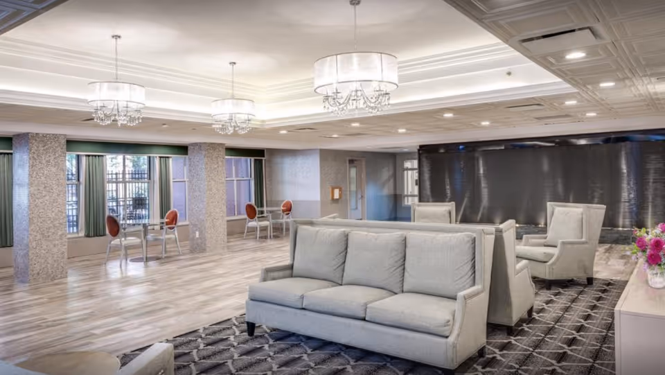 Bright, spacious lobby area with gray sofas, chairs, chandeliers, and large windows.