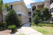 Two-story beige facility with arches, balconies, a walkway, and landscaped greenery.