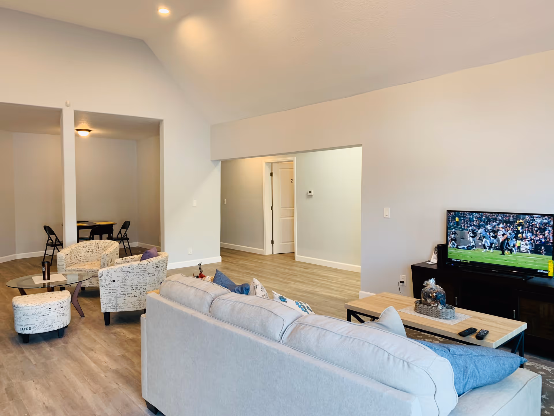 Light-filled living room with sofa, coffee table, TV, and dining nook in back