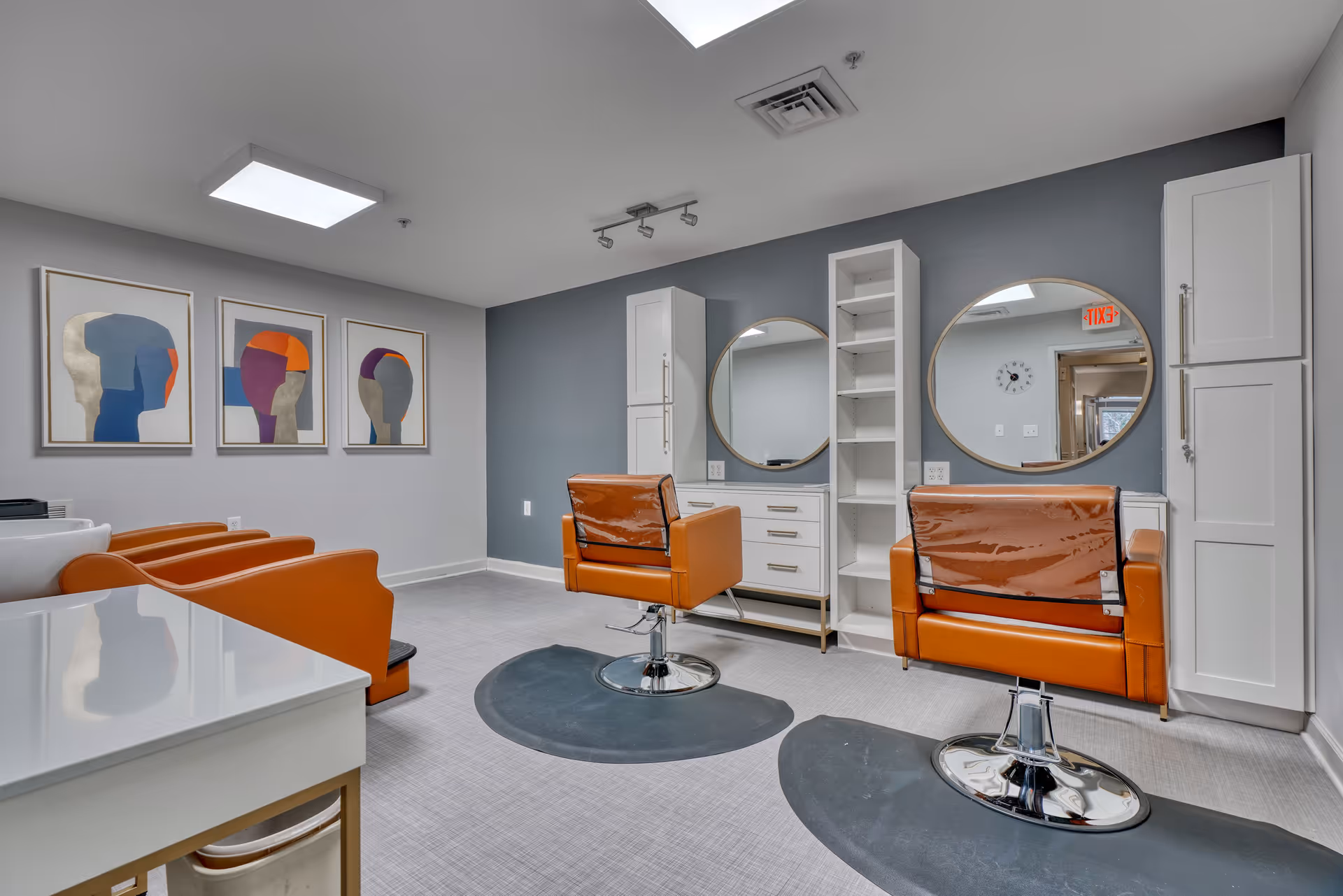 Interior salon area with orange chairs, circular mirrors, white cabinets, sinks, and blue-gray walls.
