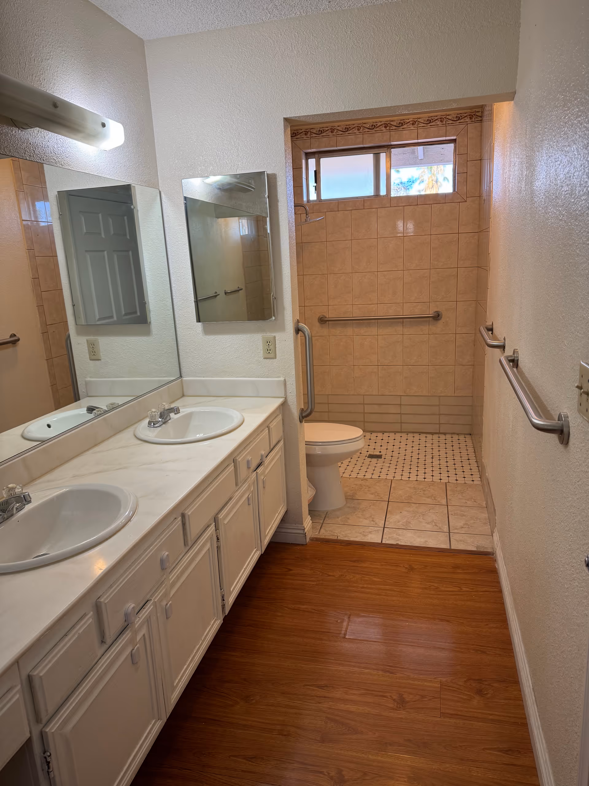 Bathroom with dual sinks, mirrors, toilet, walk-in shower, and accessibility grab bars.