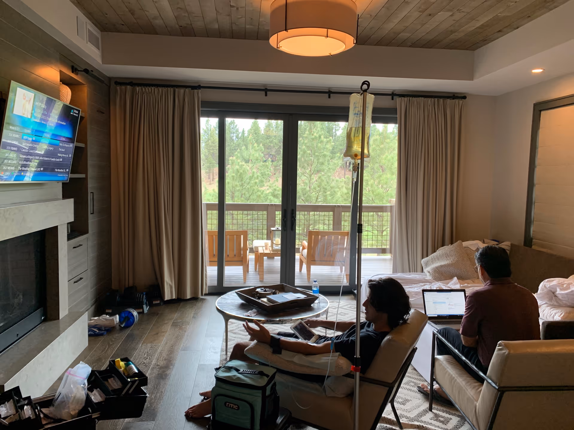 Two residents relax in a living room with an IV pole and balcony view.