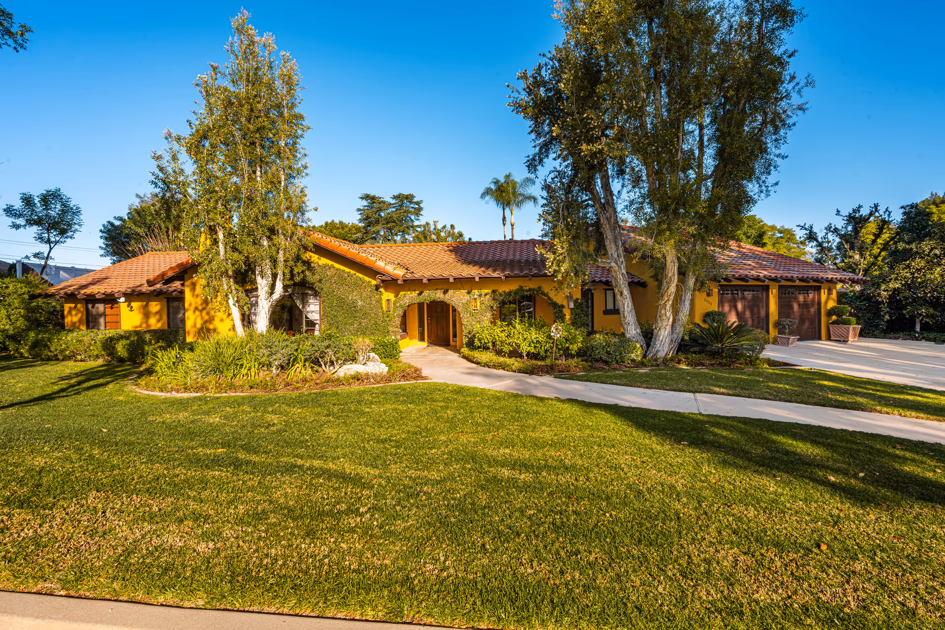A single-story yellow building with a red tile roof amid green lawn and trees.