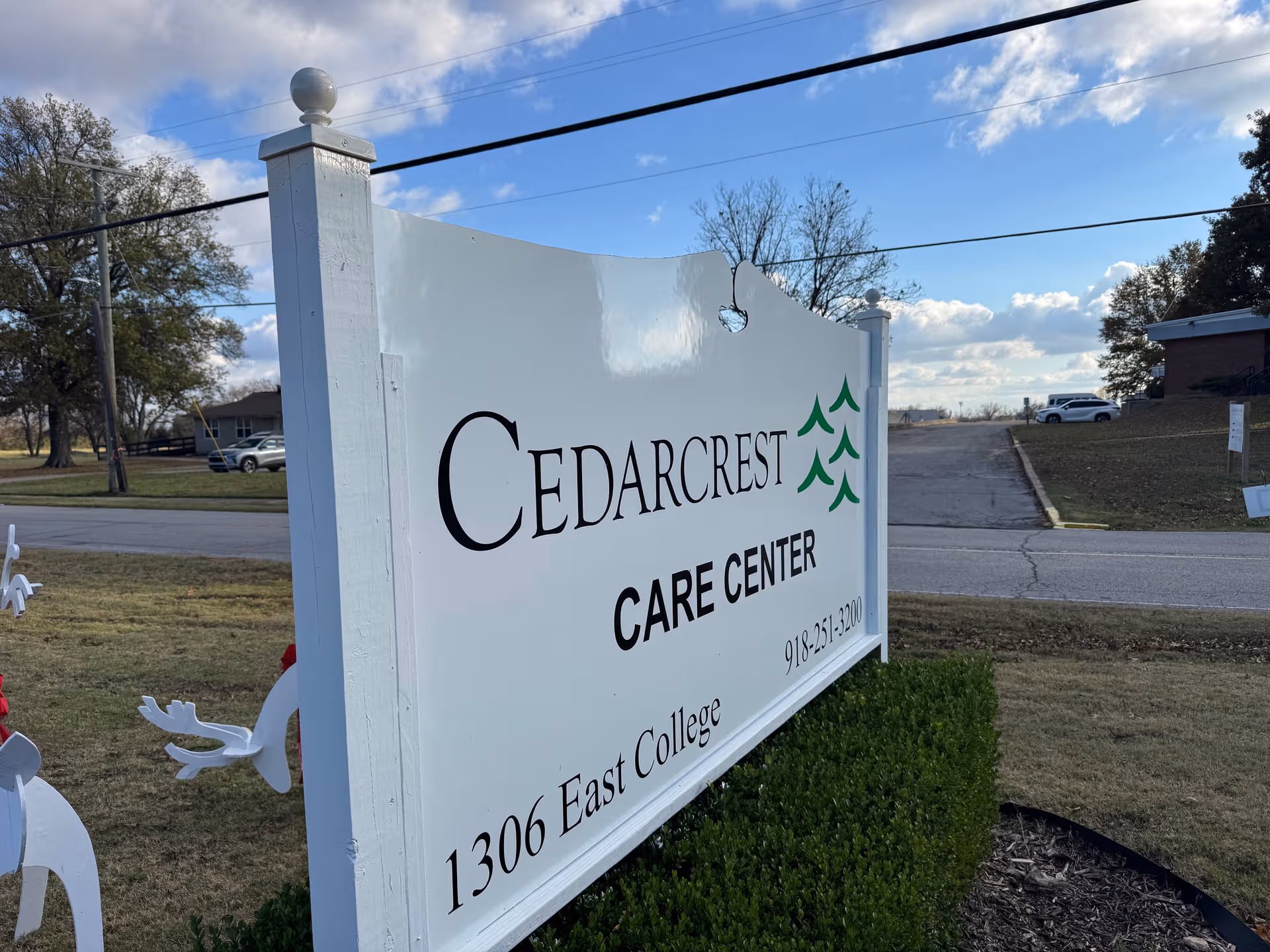 White Cedarcrest Care Center sign on a grassy lawn with a road in the background.