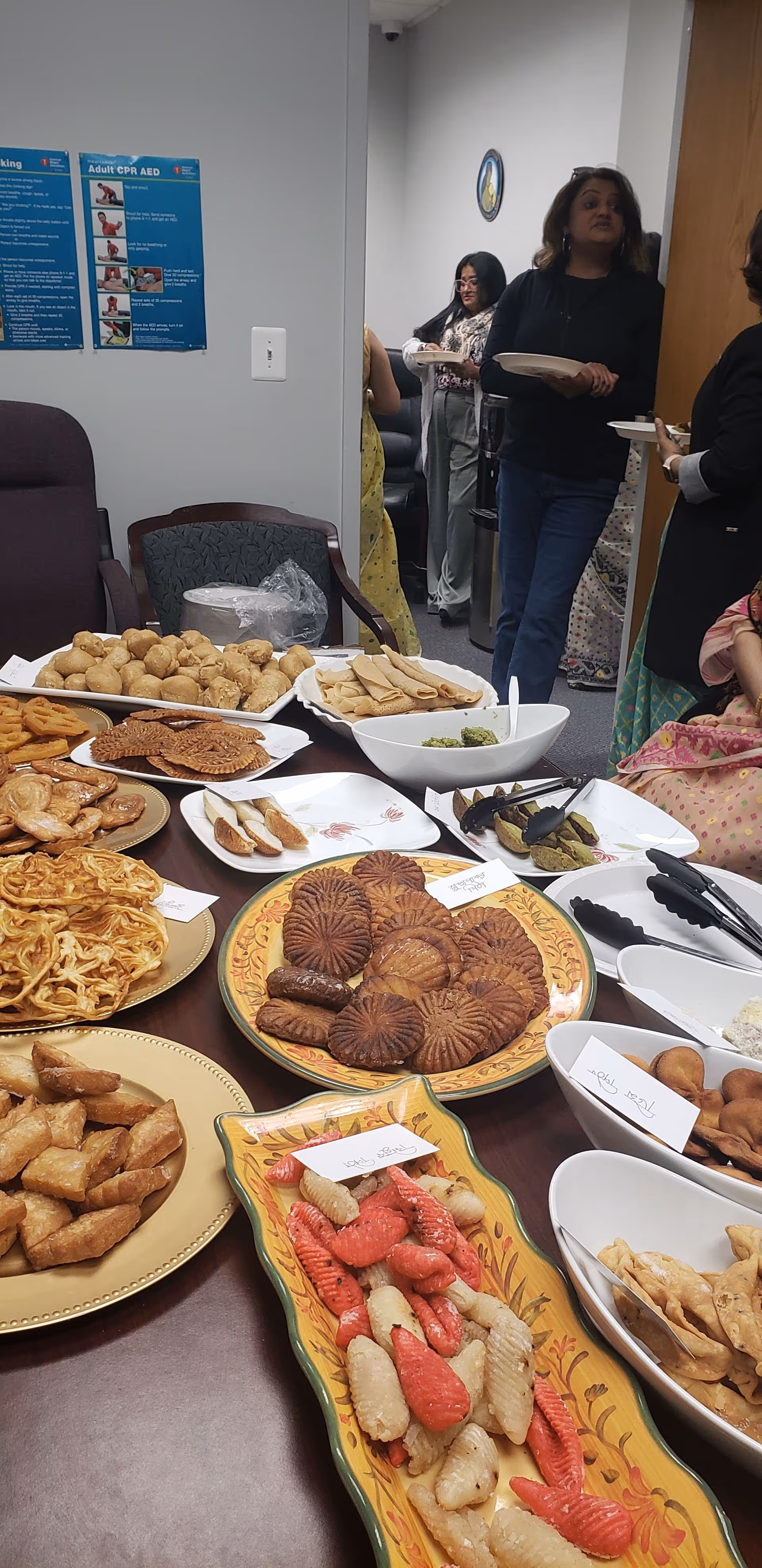 Table filled with pastries and snacks in a dining area, with people serving plates.