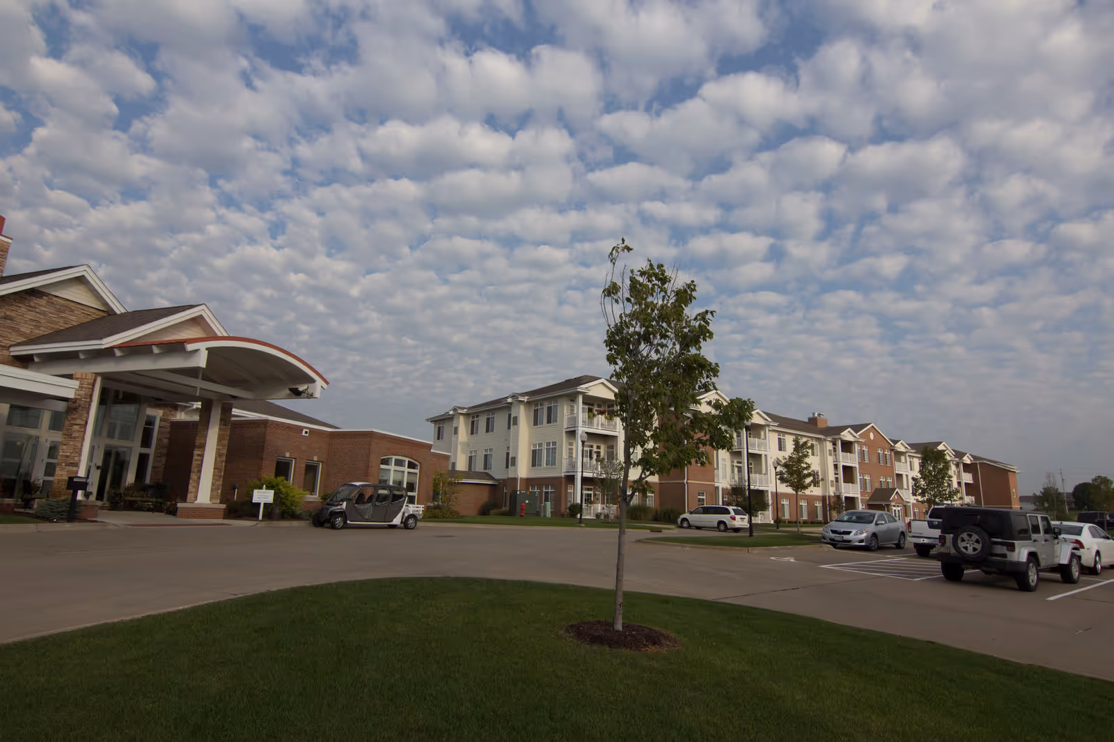 Exterior view of The Fountains senior living facility with parked cars and a curved entrance.