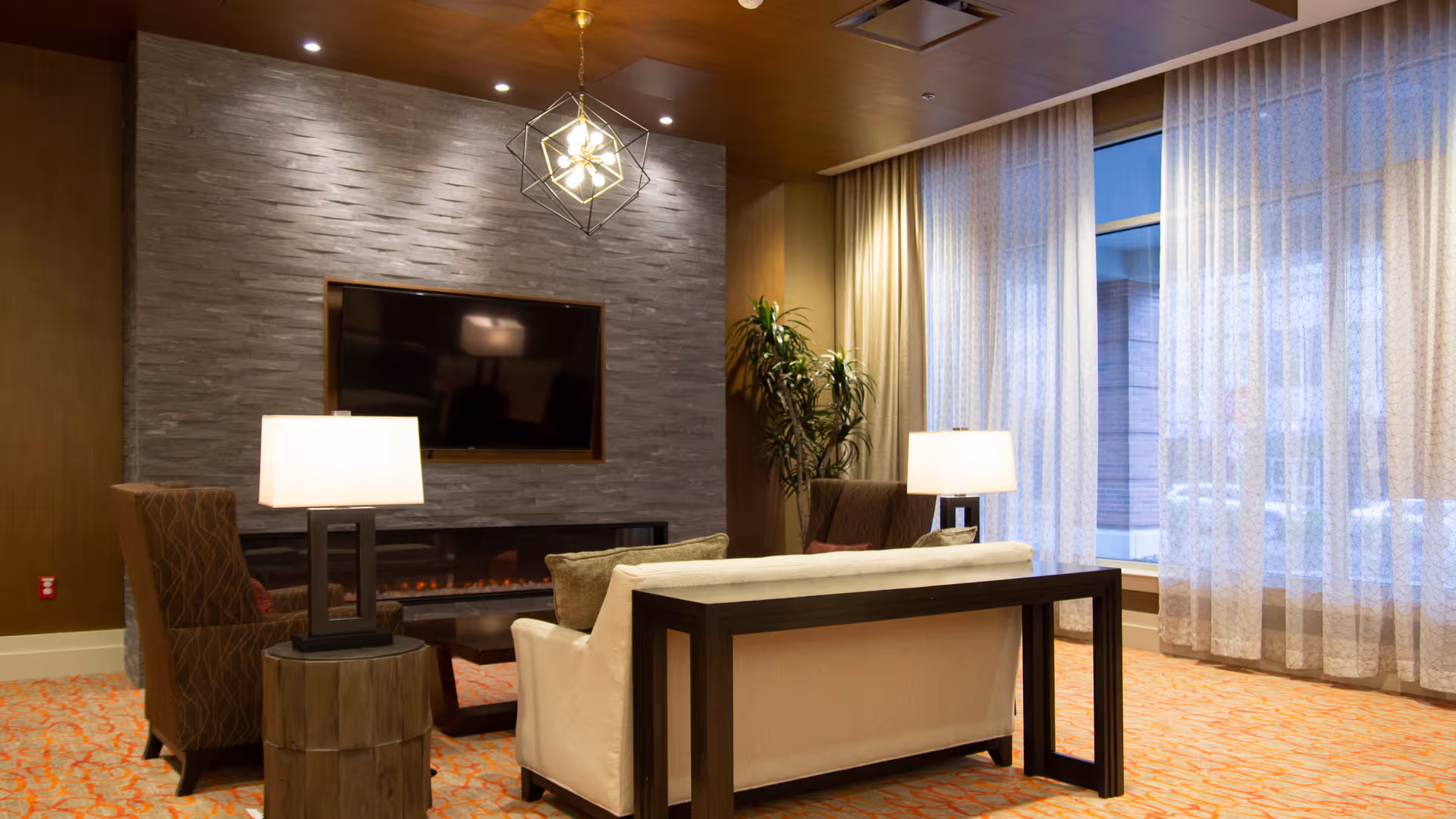 Modern lounge area with fireplace, TV, and large windows in a senior living facility.
