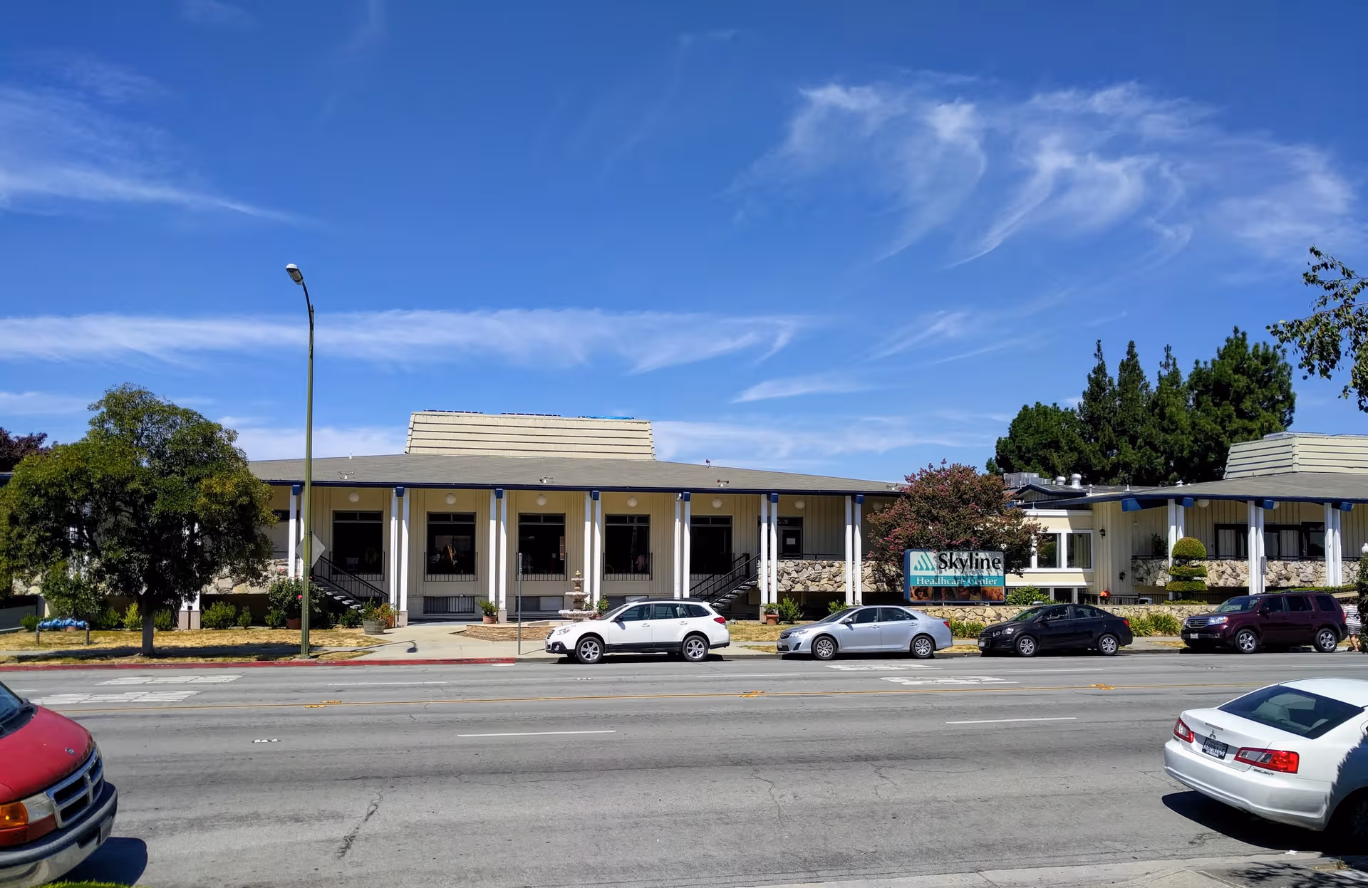Exterior view of Skyline Health Care Center along a street with parked cars.