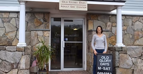 A woman stands at the stone front entrance of Old Glory Days Adult Day Center.