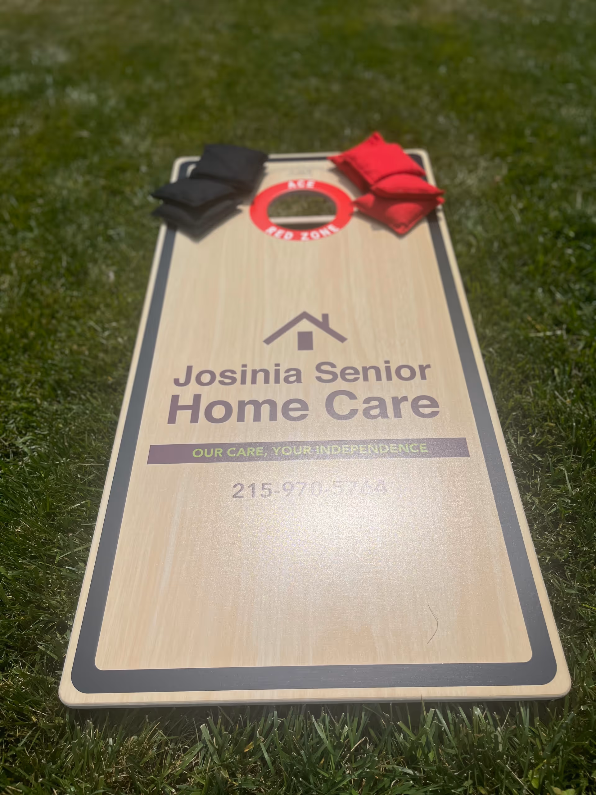 A wooden cornhole board on a grassy lawn with Josinia Senior Home Care branding.