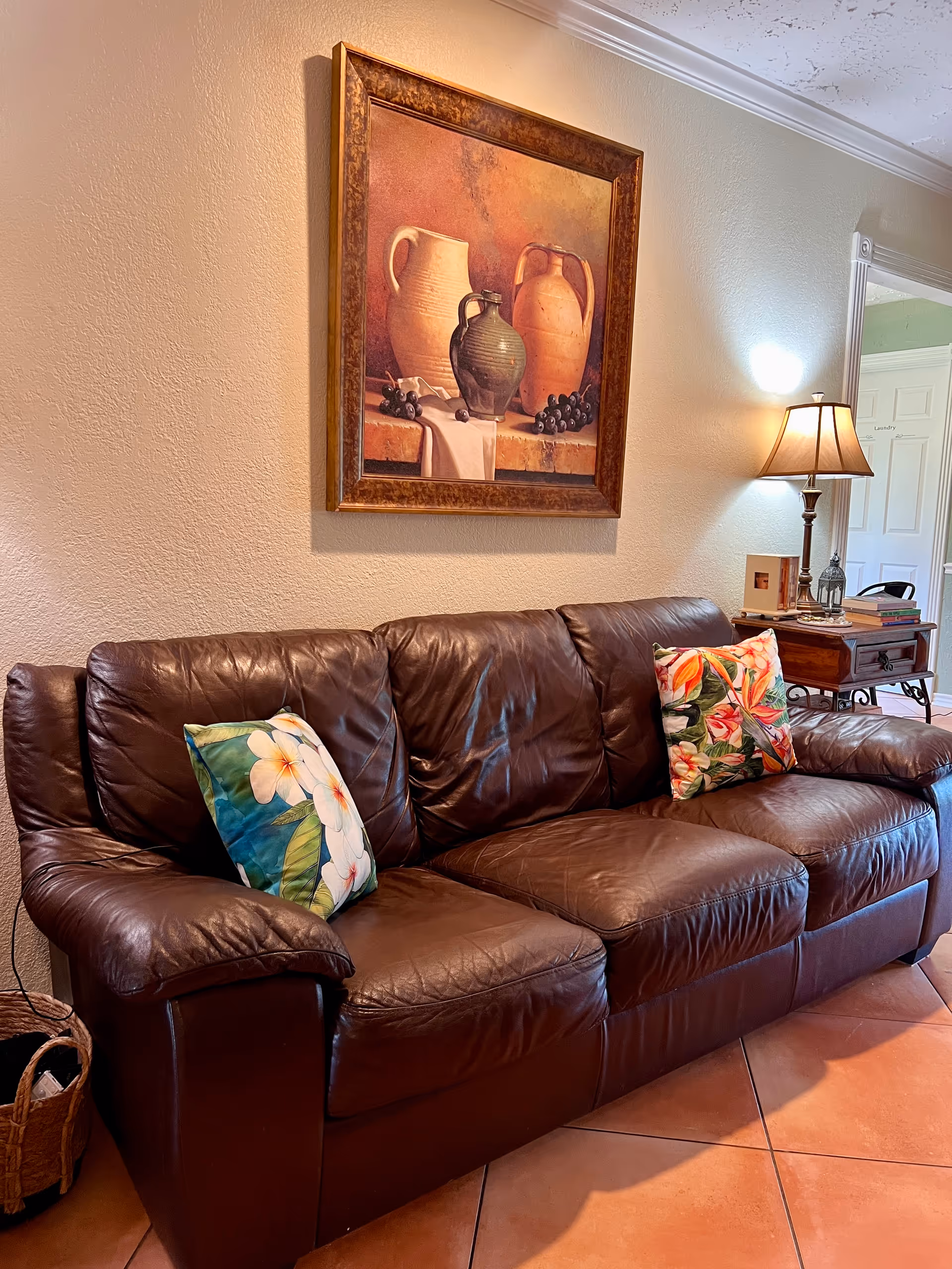 Brown leather sofa with colorful pillows sits in a cozy living room with wall art.