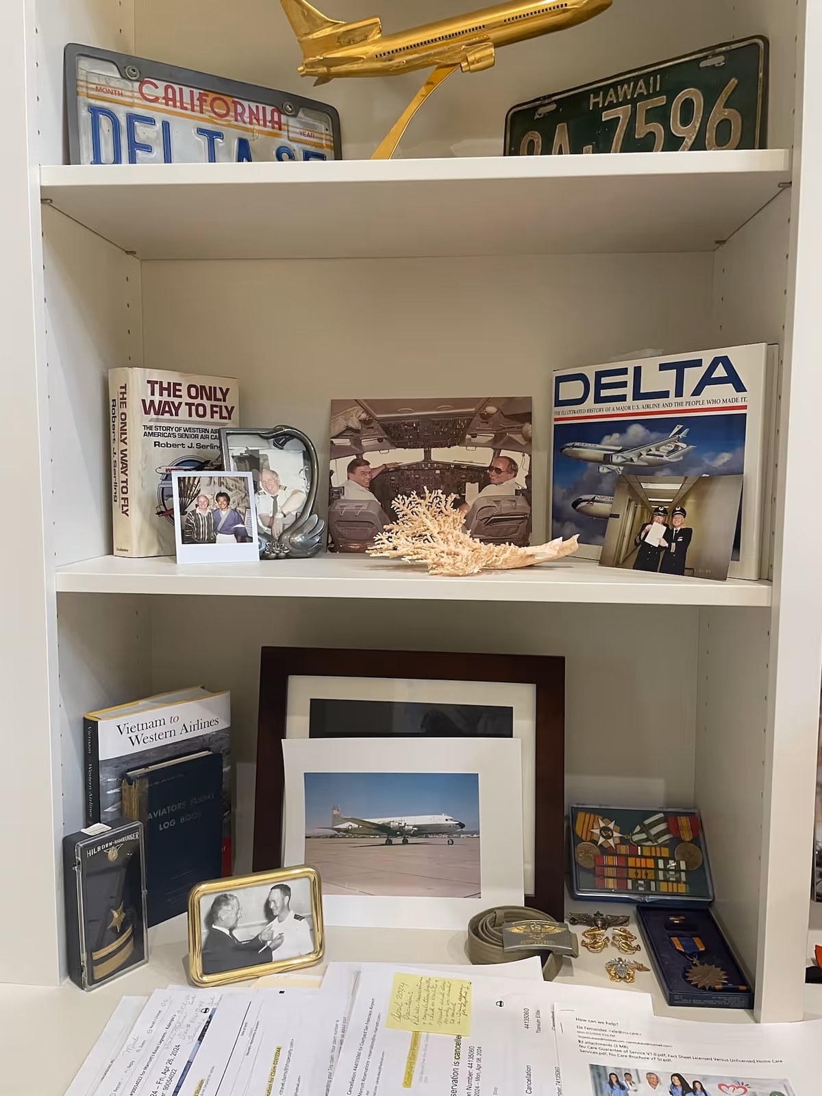 Shelf with travel memorabilia, photos, books, and a model airplane on a white cabinet.