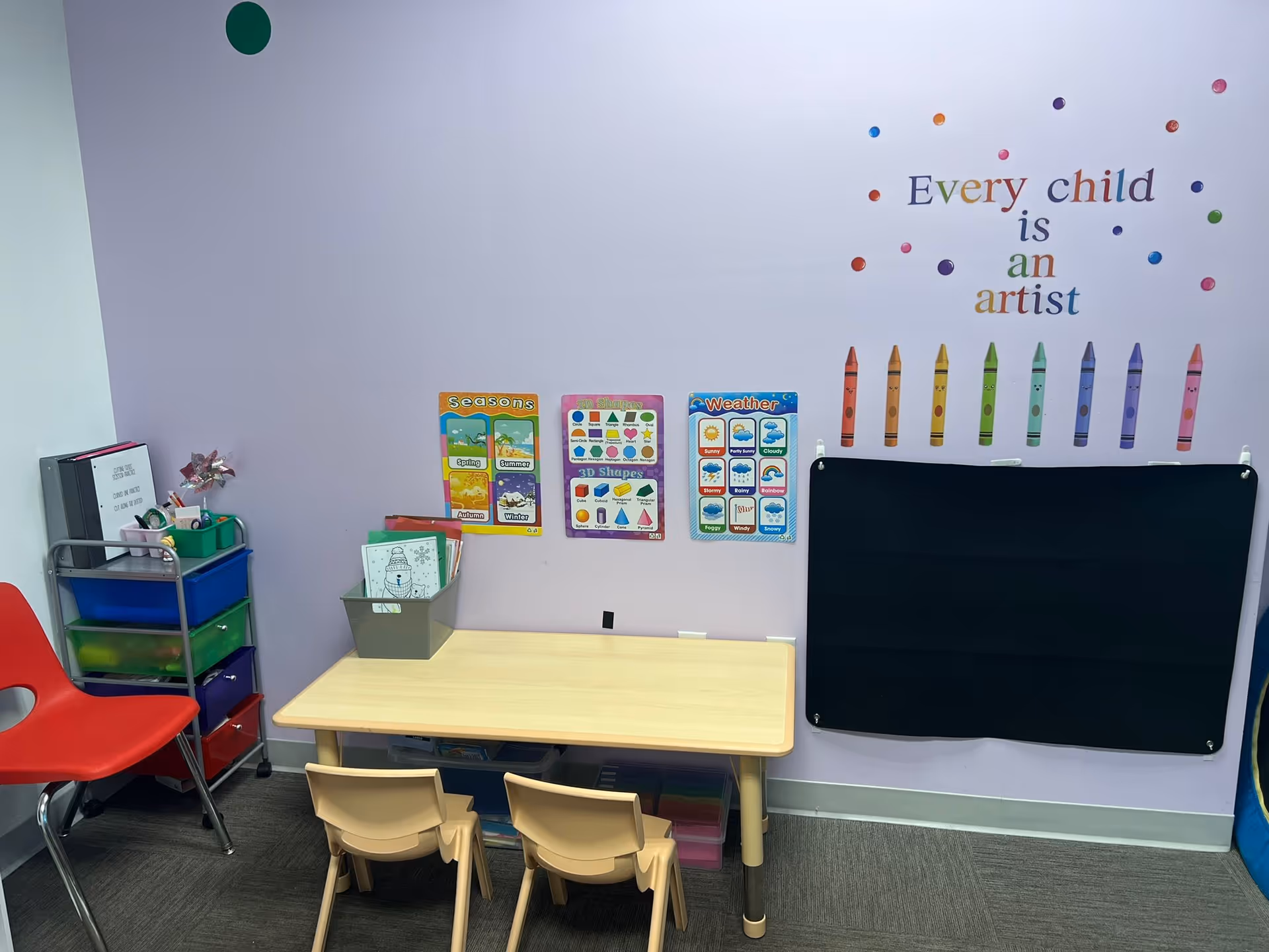 A small classroom corner with a table, chairs, colorful wall decals, and storage bins.