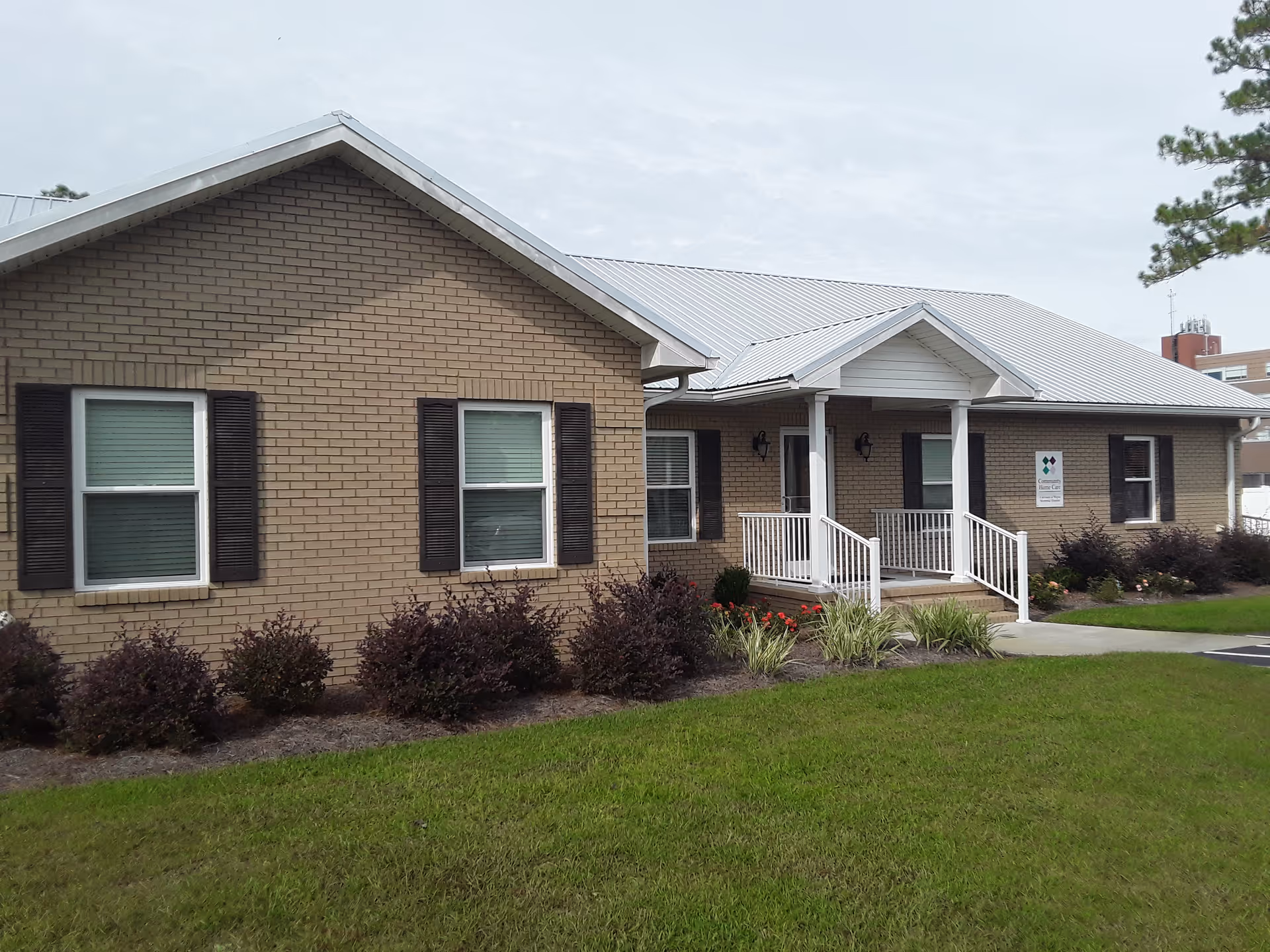 Exterior view of a single-story brick senior home with a white porch and landscaping.