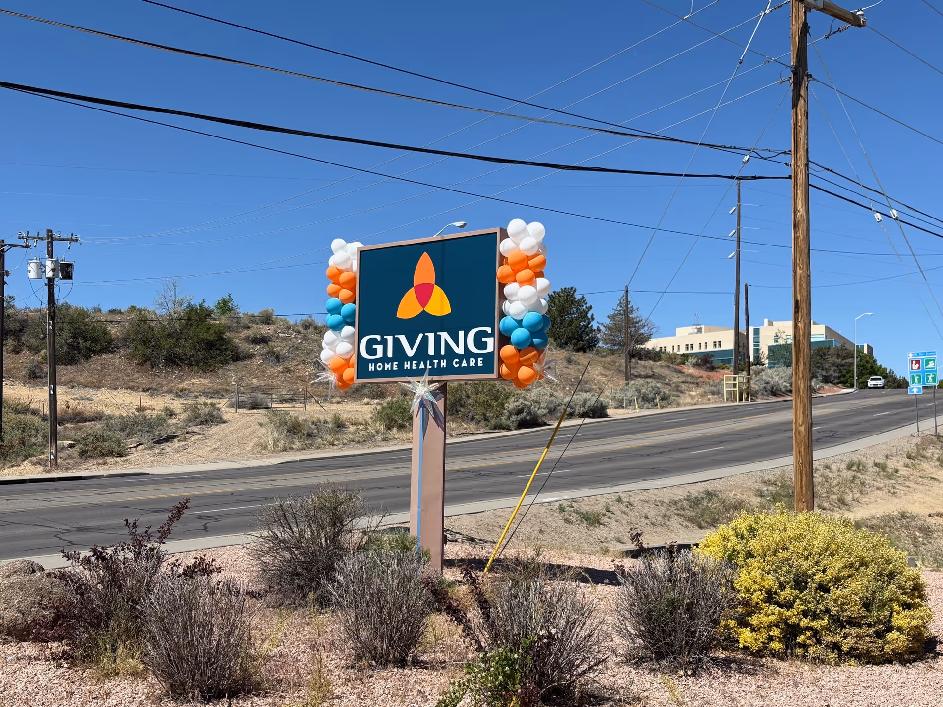 Roadside view of a Giving Home Health Care sign adorned with orange and white balloons.