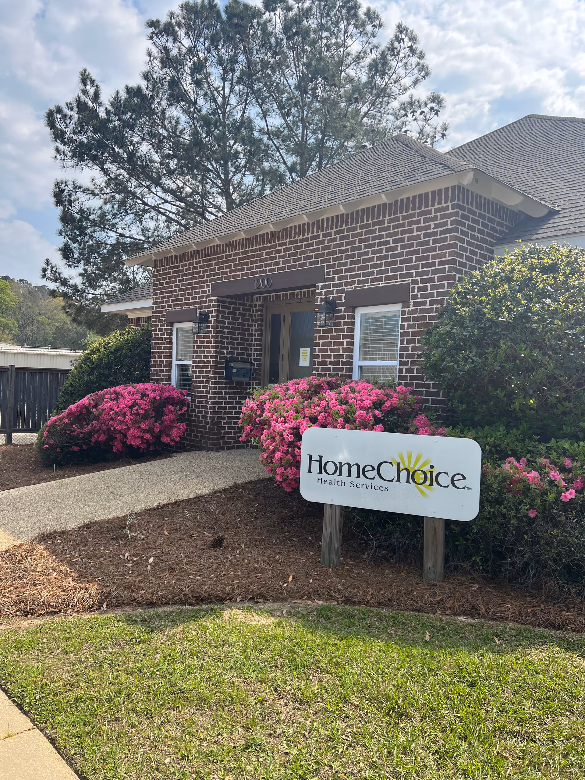 Brick facility entrance with a HomeChoice Health Services sign beside pink flowers.