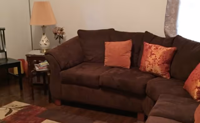Brown sectional sofa with orange cushions in a cozy living room with a lamp.