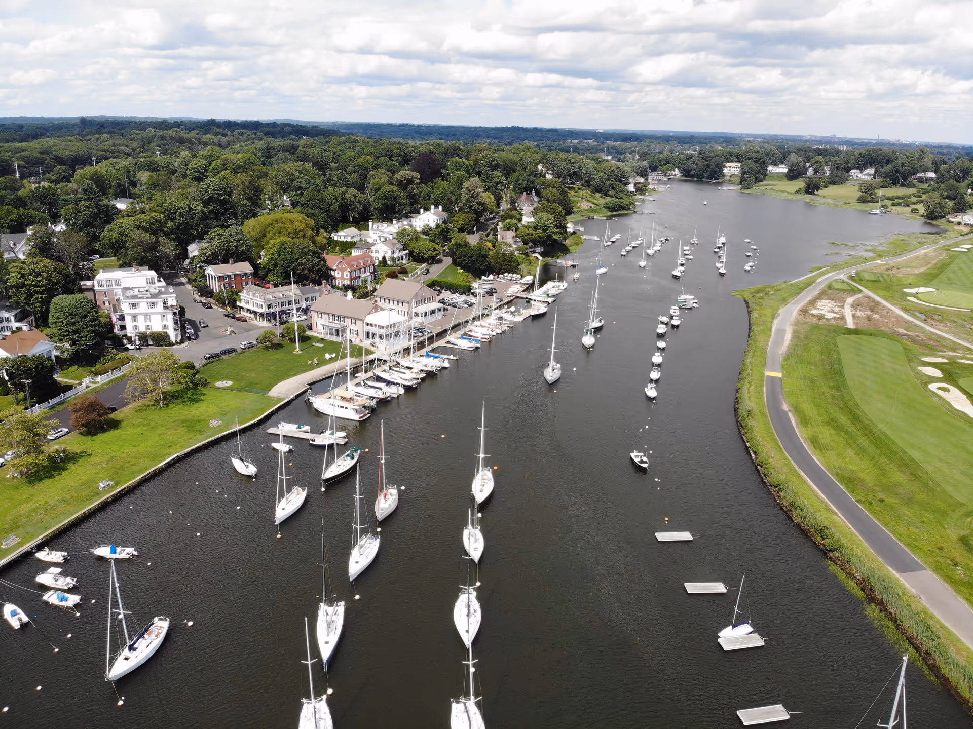 Aerial view of a marina town with boats, water, and green shoreline.