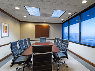 A long conference table with black chairs in a bright boardroom.