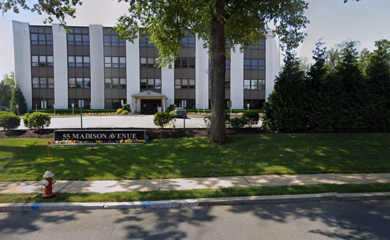 Exterior view of a white multi-story building with a green lawn and sidewalk.
