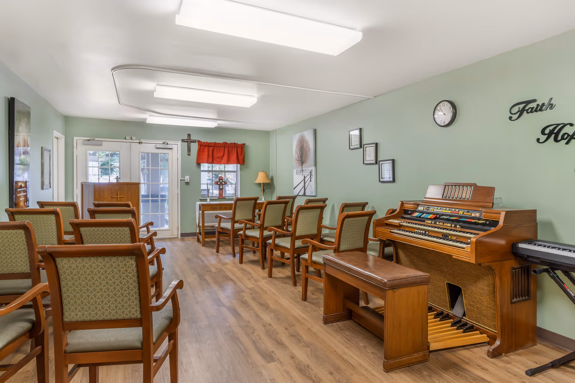 Senior living common room with chairs facing an organ console against a green wall.