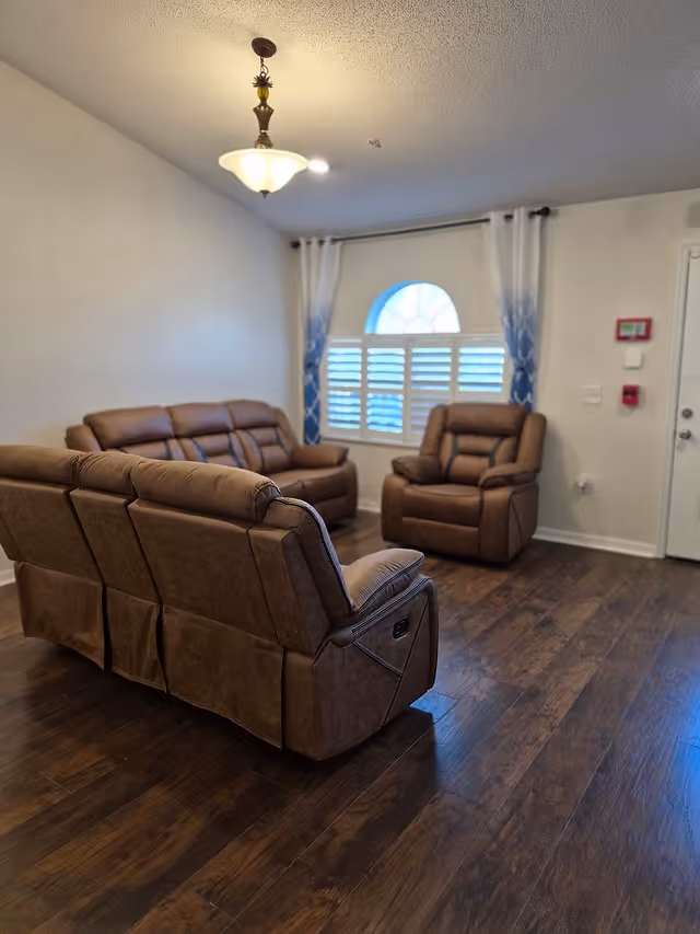 Brown leather seating area with a sofa and two recliners in a living room.