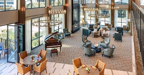A spacious senior living lobby features seating clusters, a grand piano, and large windows.