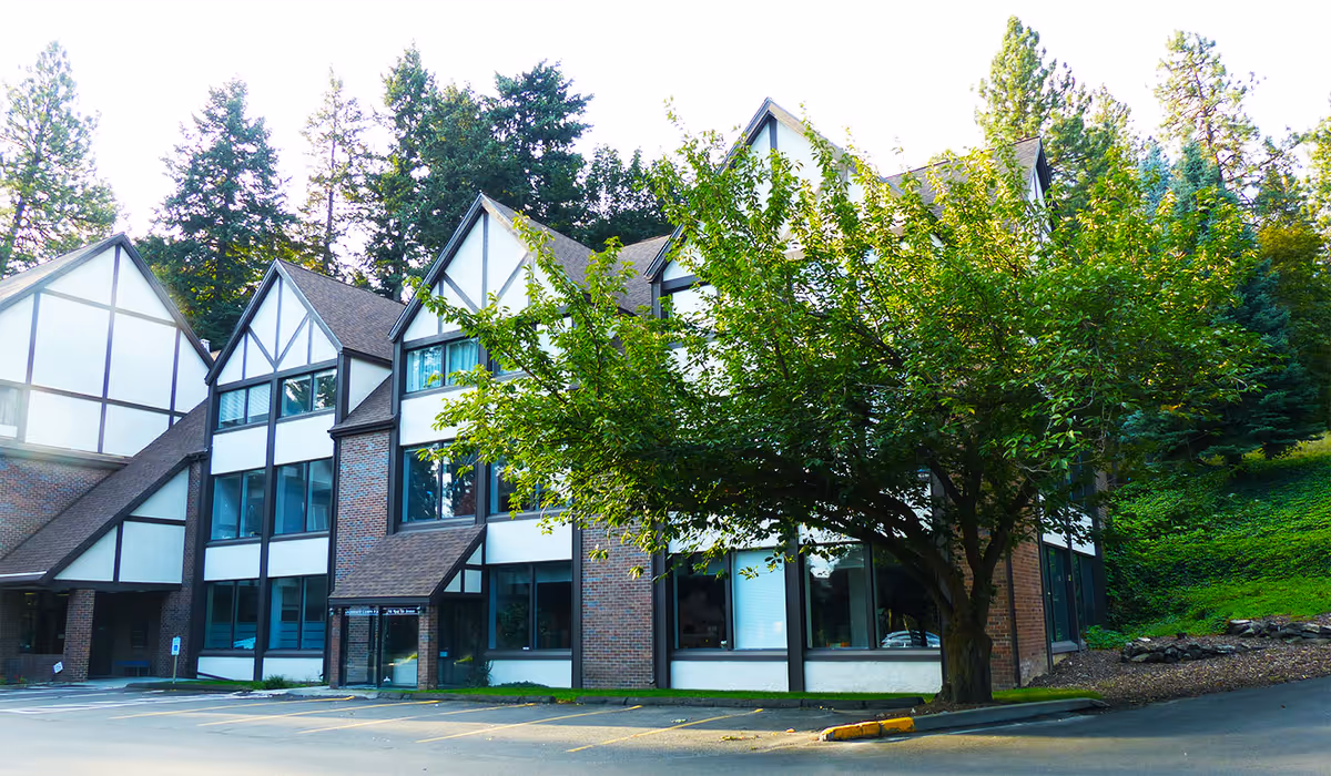 Exterior view of a senior living facility with a large tree in front.