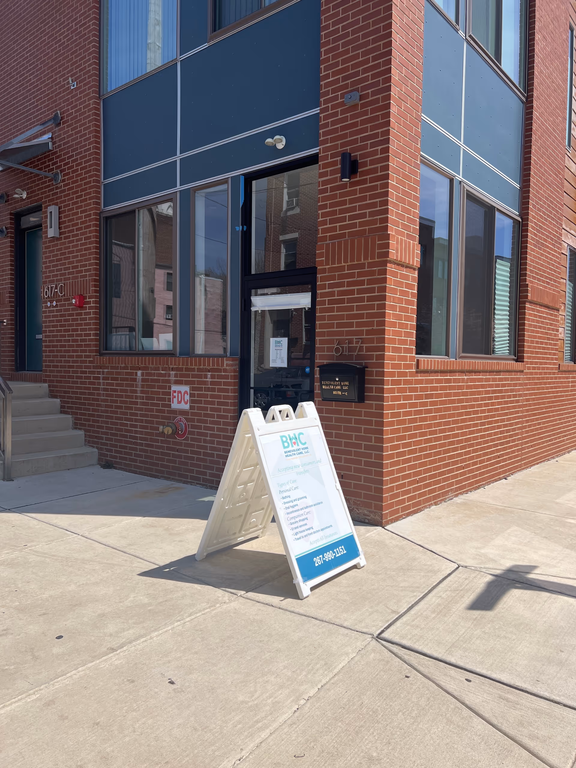 Exterior brick building entrance with glass doors and an A-frame sidewalk sign.