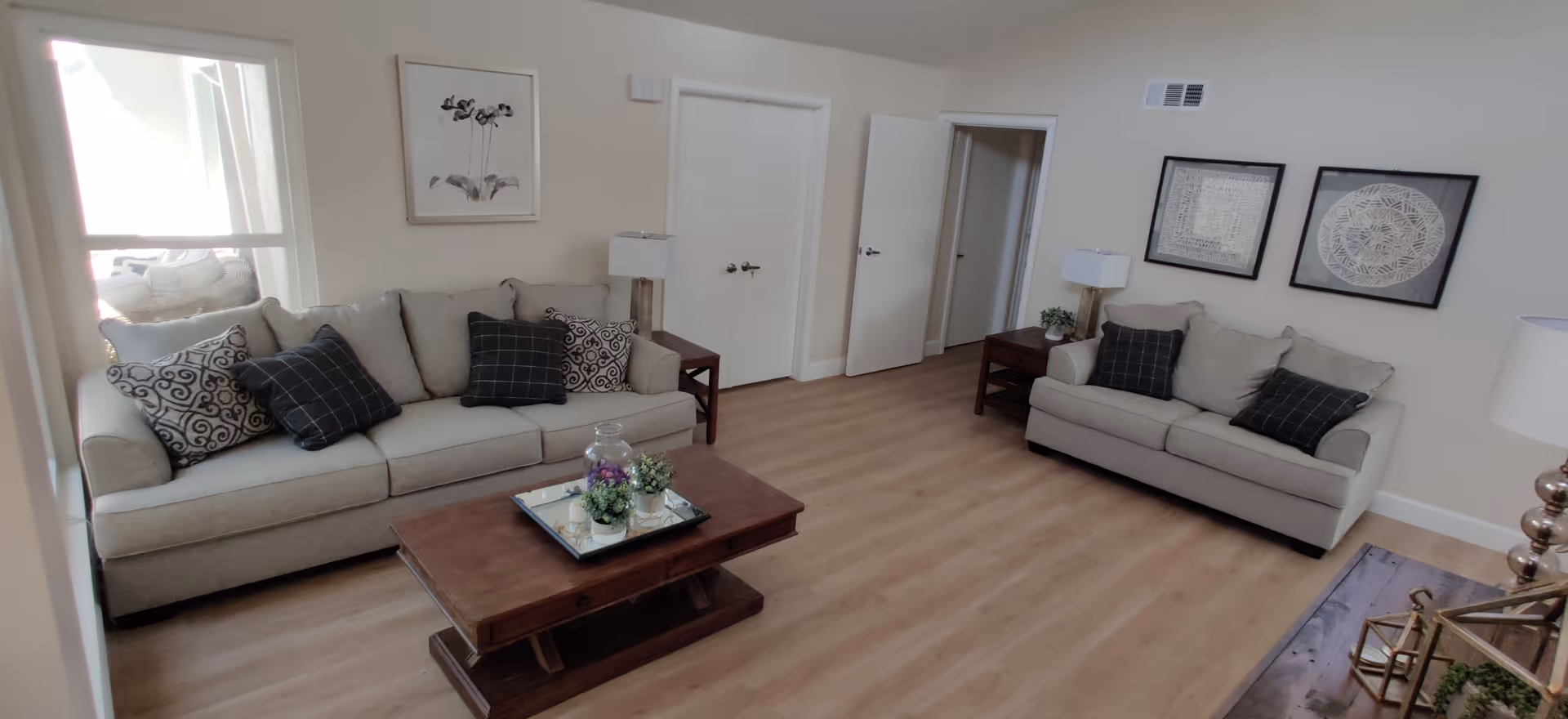 Bright shared living room with two beige sofas, coffee table, and wall art.