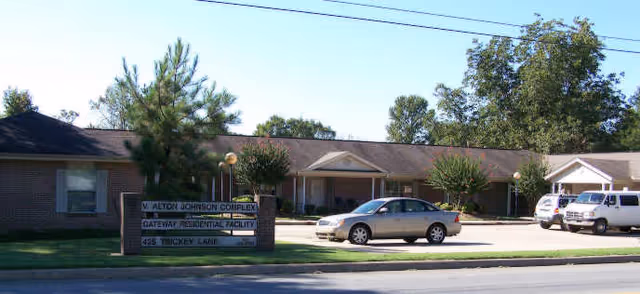Exterior view of Pathfinder, Inc. V. Alton Johnson Apartments facility with sign, driveway, and parked cars.