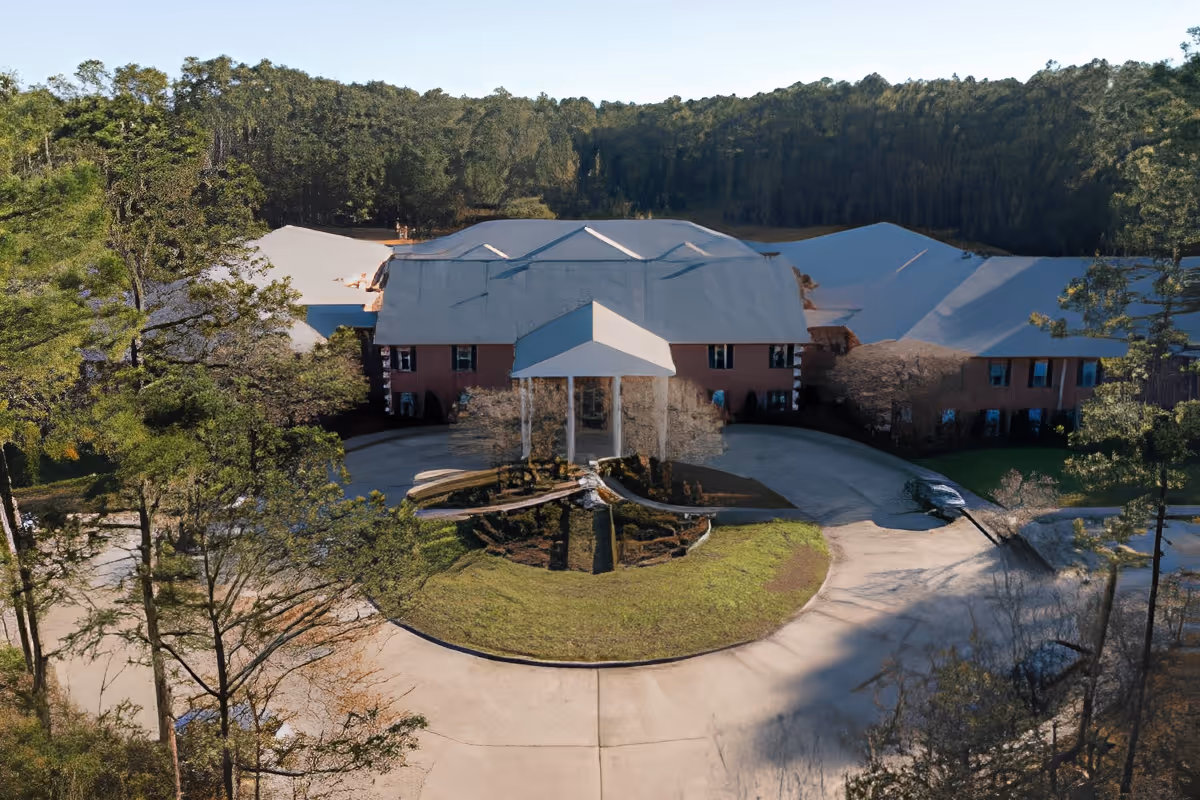 Aerial view of the SummerHouse Park Provence building front with a covered entrance, circular driveway and fountain surrounded by trees.
