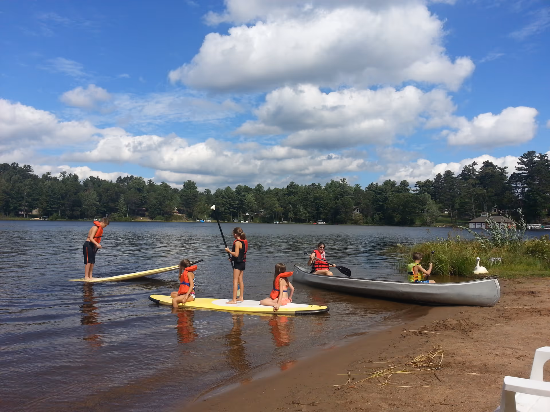 People paddleboarding and canoeing on a lake under a blue sky.