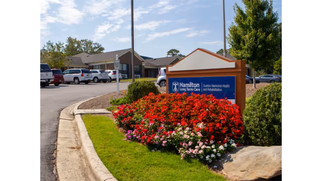 Front exterior of a senior care facility with a colorful flower bed and sign.