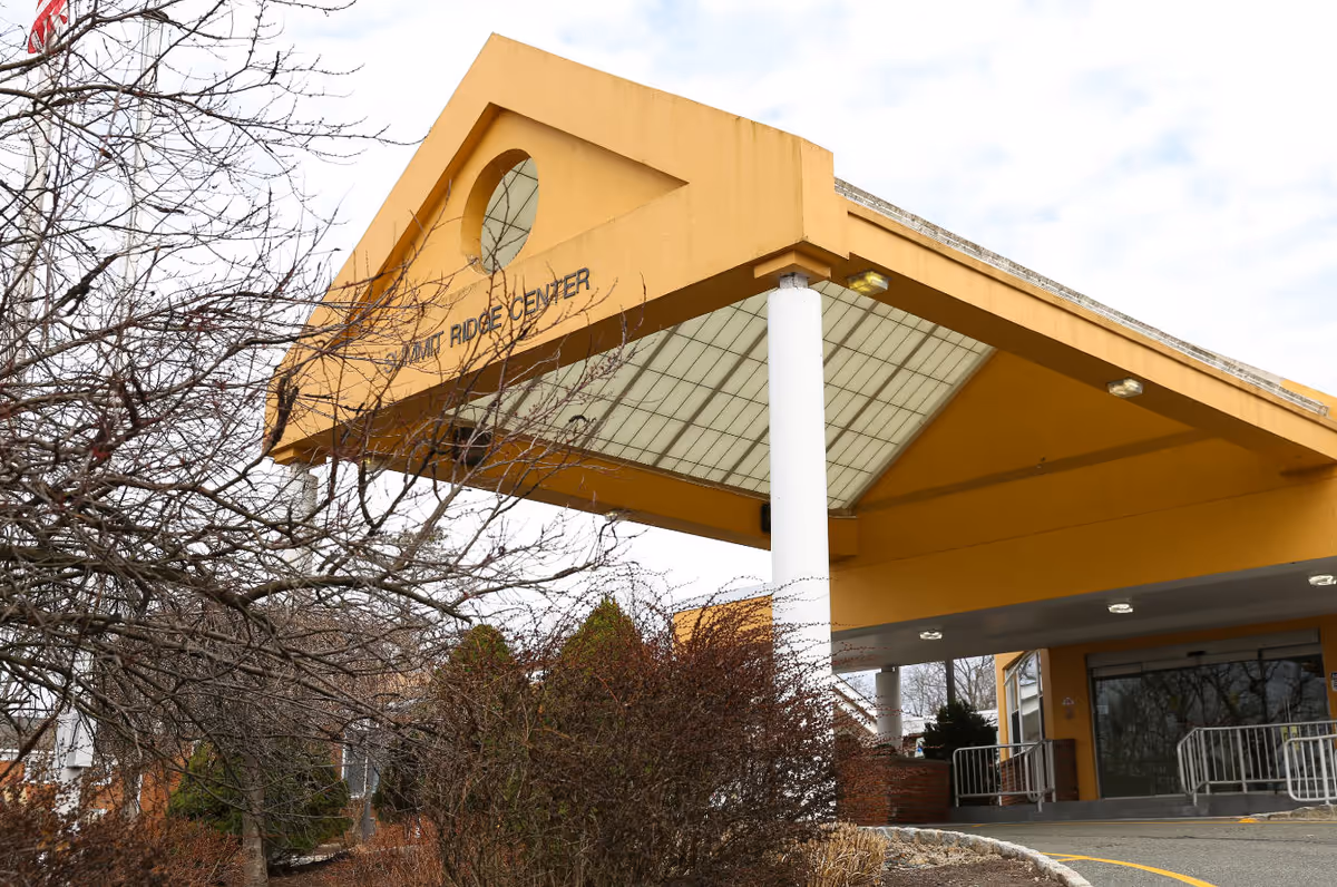 Exterior view of a yellow facility entrance with a covered drop-off and white column