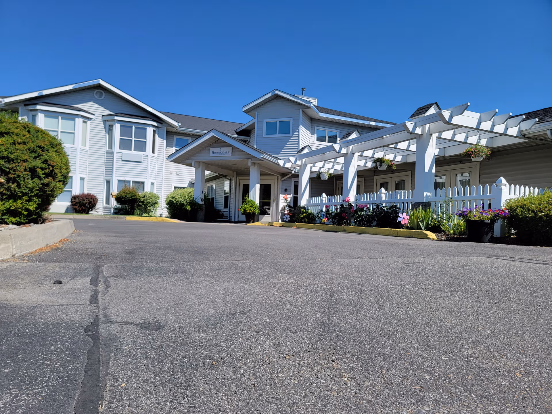 Exterior view of Brookdale Coeur d'Alene showing a white building, pergola, and flower beds.