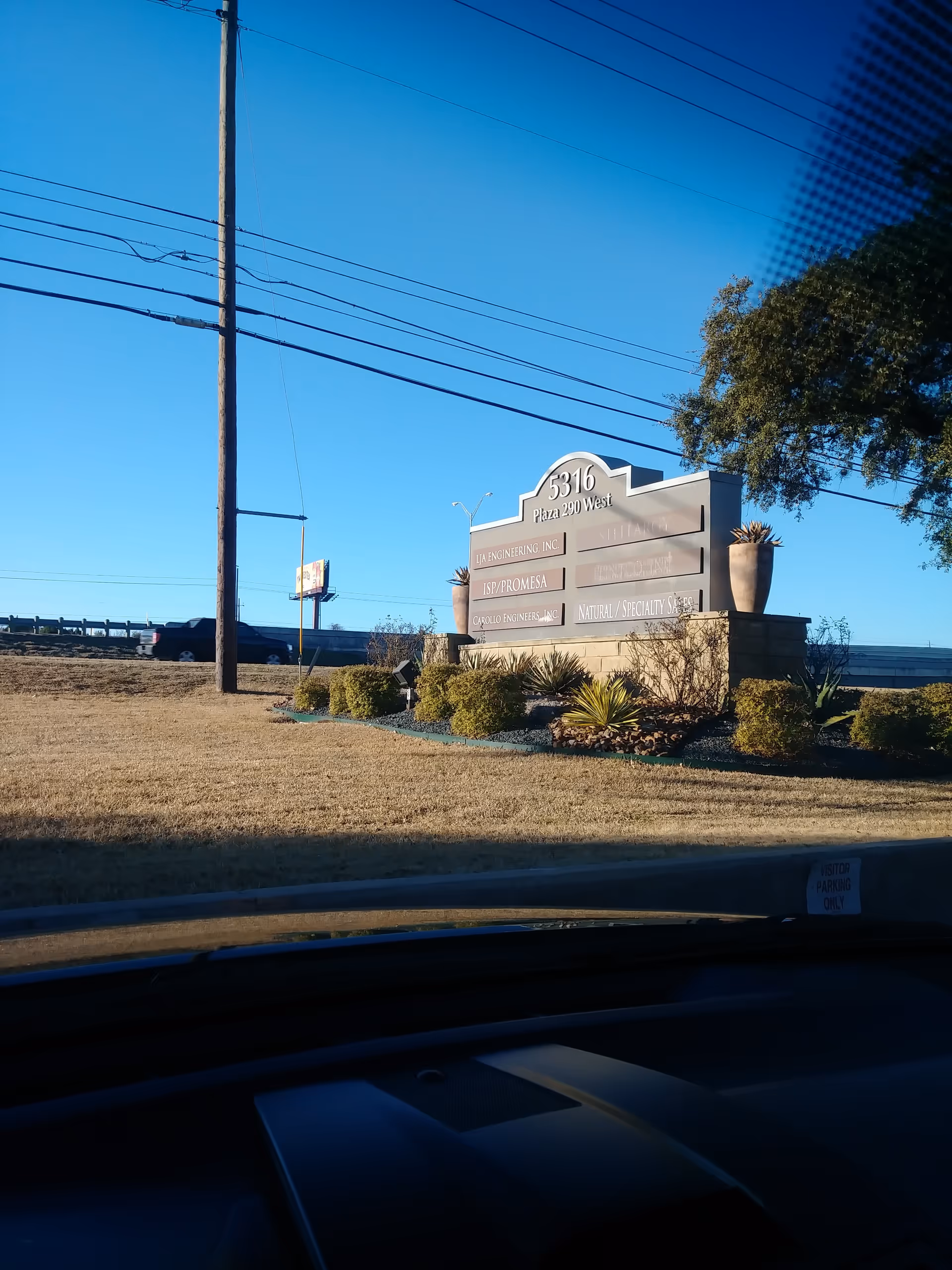 Exterior roadside sign with landscaping and power lines beside a grassy curb