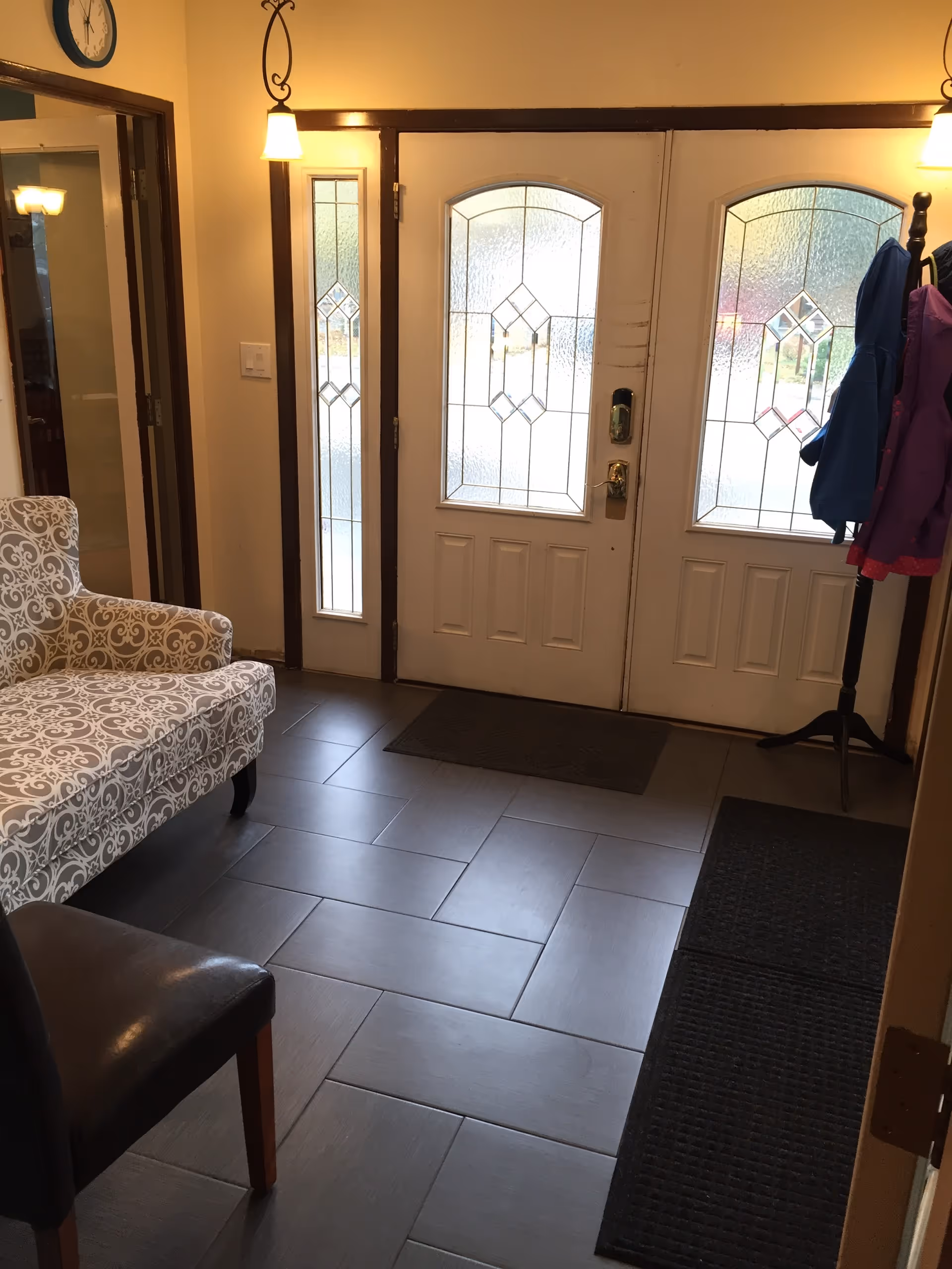 Bright foyer with patterned sofa, coat rack, and frosted glass doors at entrance.
