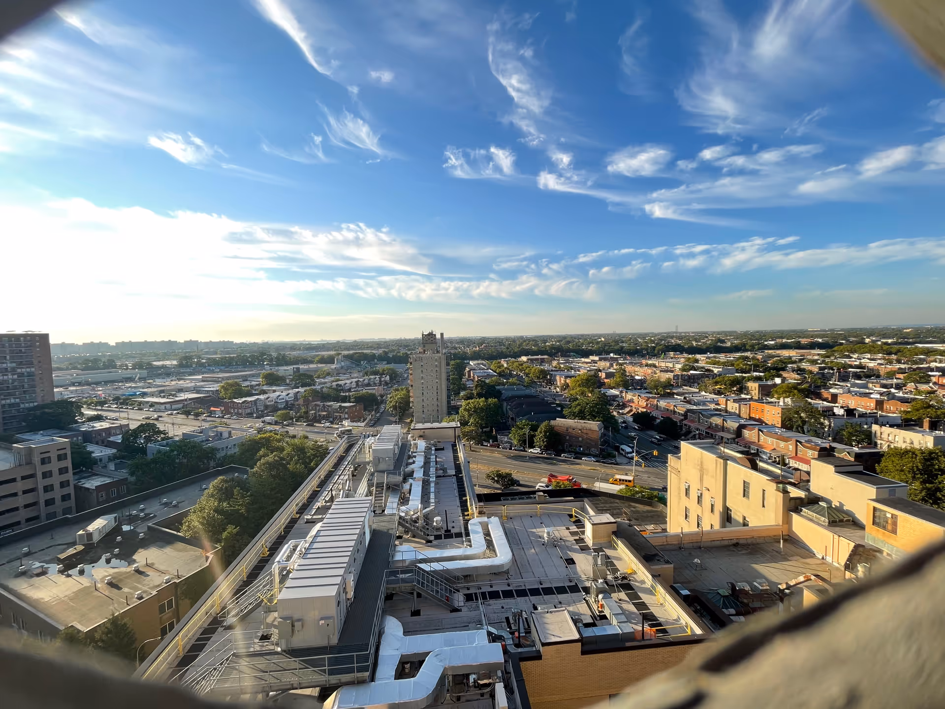 A high-angle rooftop cityscape with streets, buildings, and a clear blue sky.