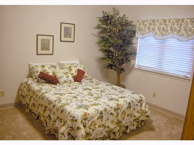 A floral-patterned bed in a cozy bedroom with a plant, window, and framed art.