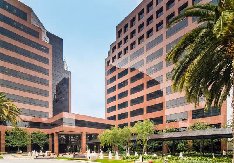 Generations Healthcare campus exterior with red-brick towers, glass windows, palm trees, and landscaped courtyard.