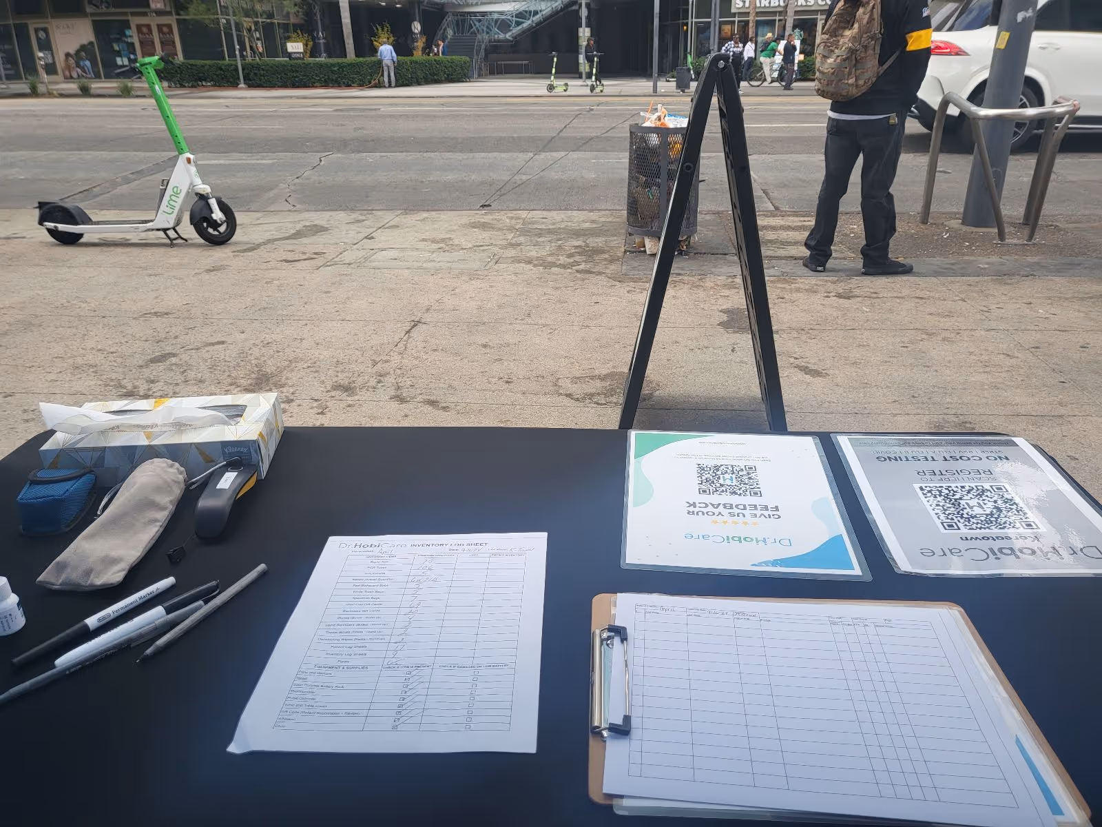 Outdoor registration table on a sidewalk with medical forms and pens.