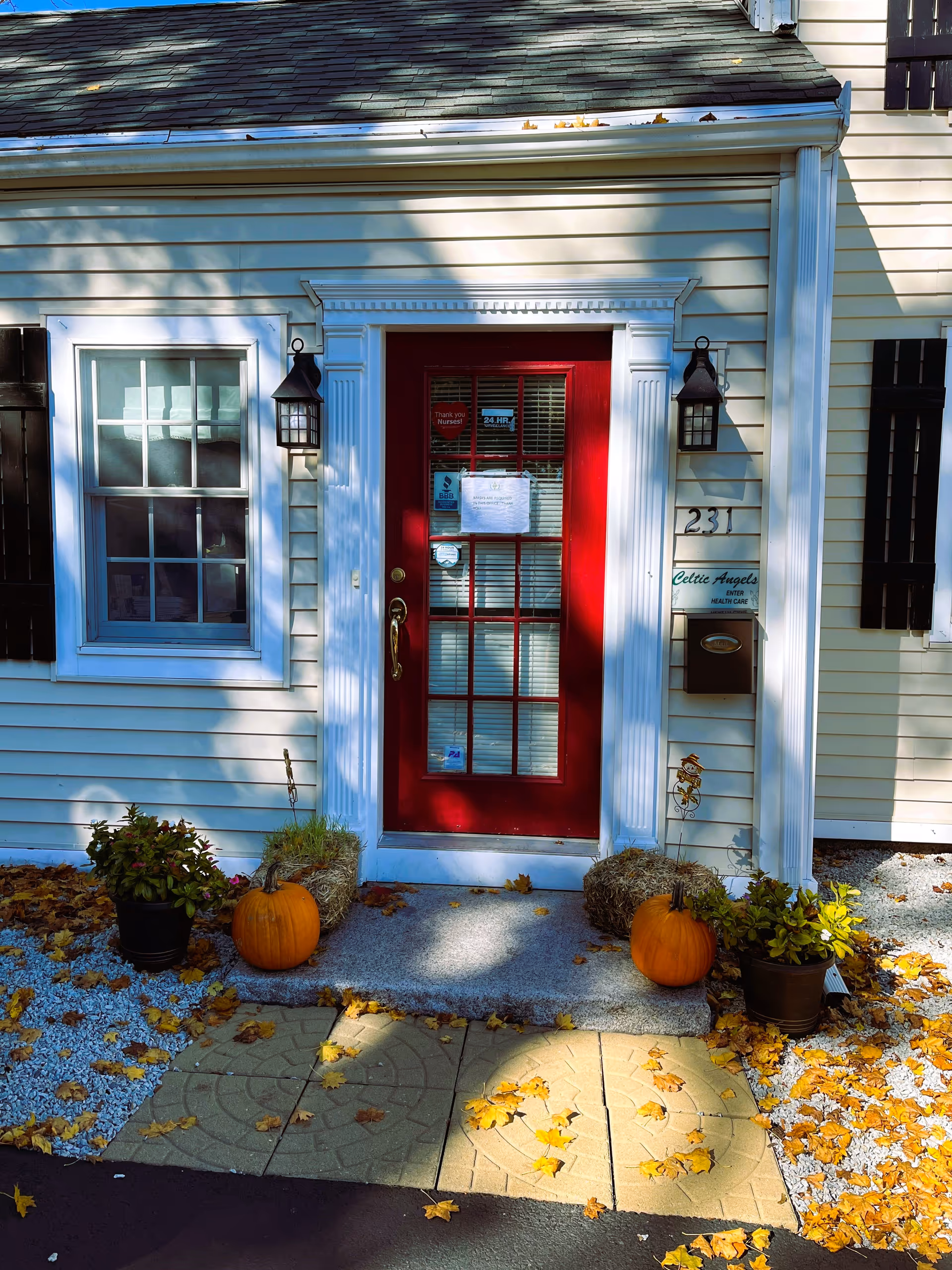 Front entrance of a beige building with a red door, pumpkins, leaves, and Celtic Angels signage.